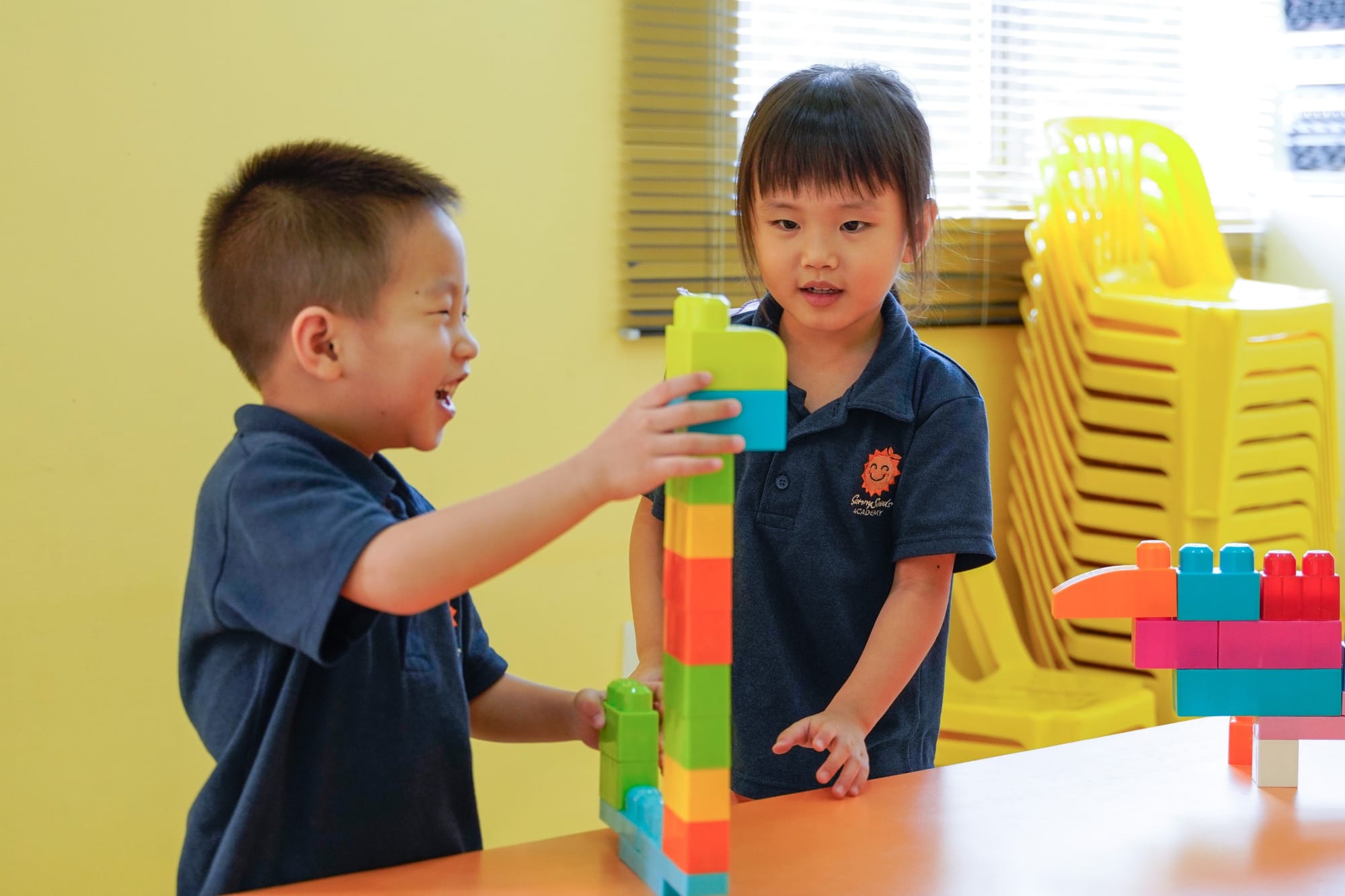 Two nursery children laughing as they build a tower of blocks